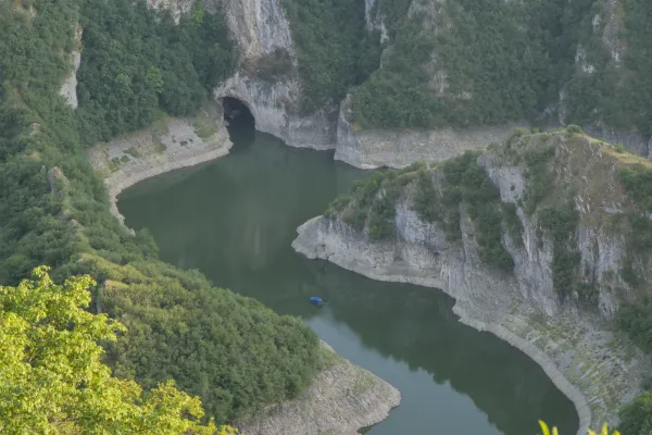 Der Uvac Canyon in Serbien zeigt verschlungene Flusswindungen und die Ušačka Höhle, mit einem kleinen blauen Boot im Wasser.