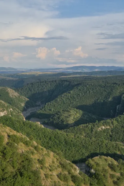 Ein verschlungener Canyon in Serbien, beleuchtet vom sanften Licht des Sonnenuntergangs, mit grünen Hügeln und einem Fluss.