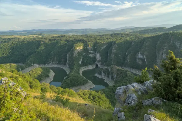 Panoramski pogled na vijugavu klisuru Uvac u Srbiji, okruženu bujnim zelenim šumama i stenovitim formacijama.