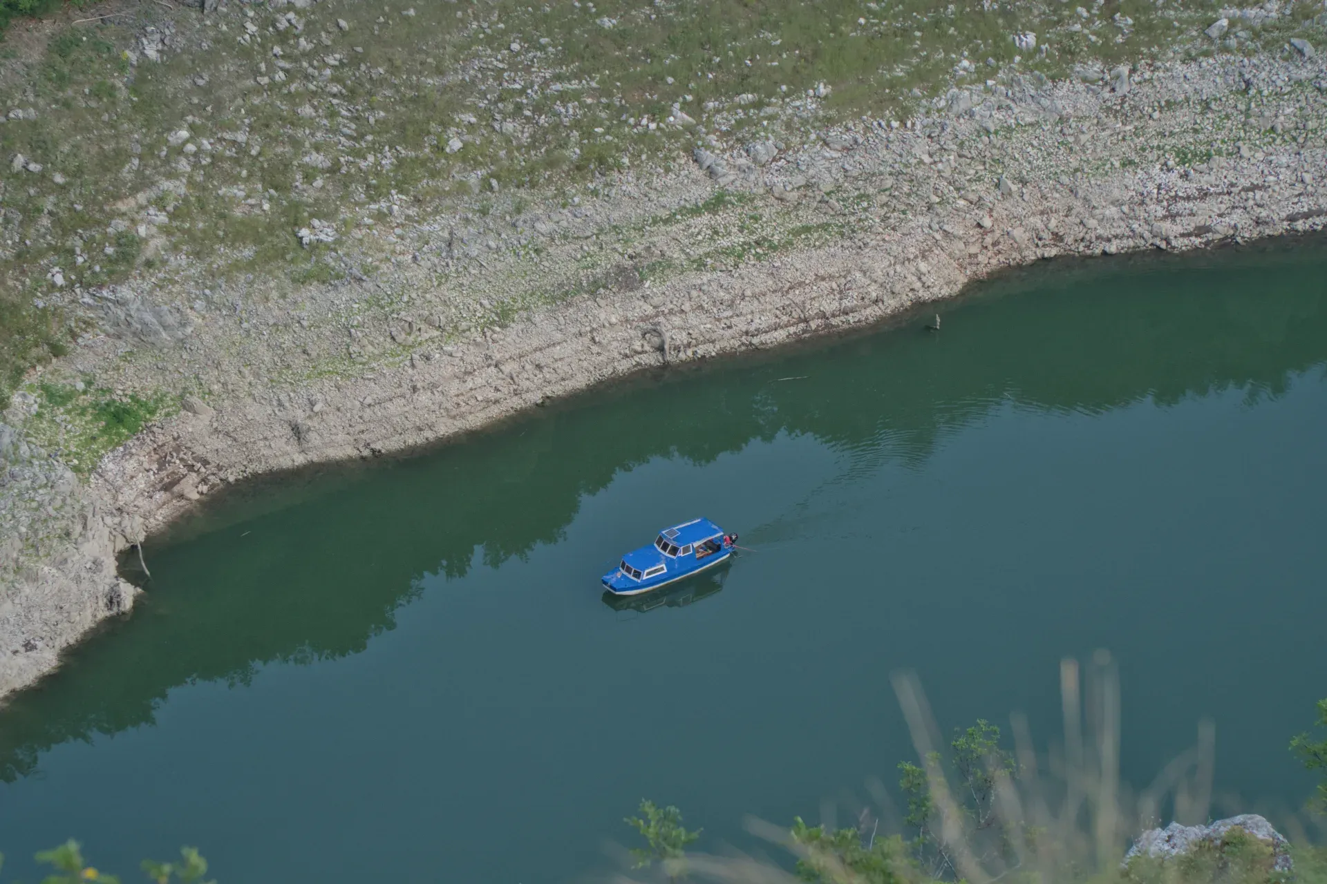 A blue excursion boat travels through the Uvac Gorge, surrounded by rocky banks and deep green water.