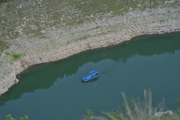 Ein blaues Ausflugsboot fährt durch die Uvac-Schlucht, umgeben von felsigen Ufern und tiefem, grünem Wasser.