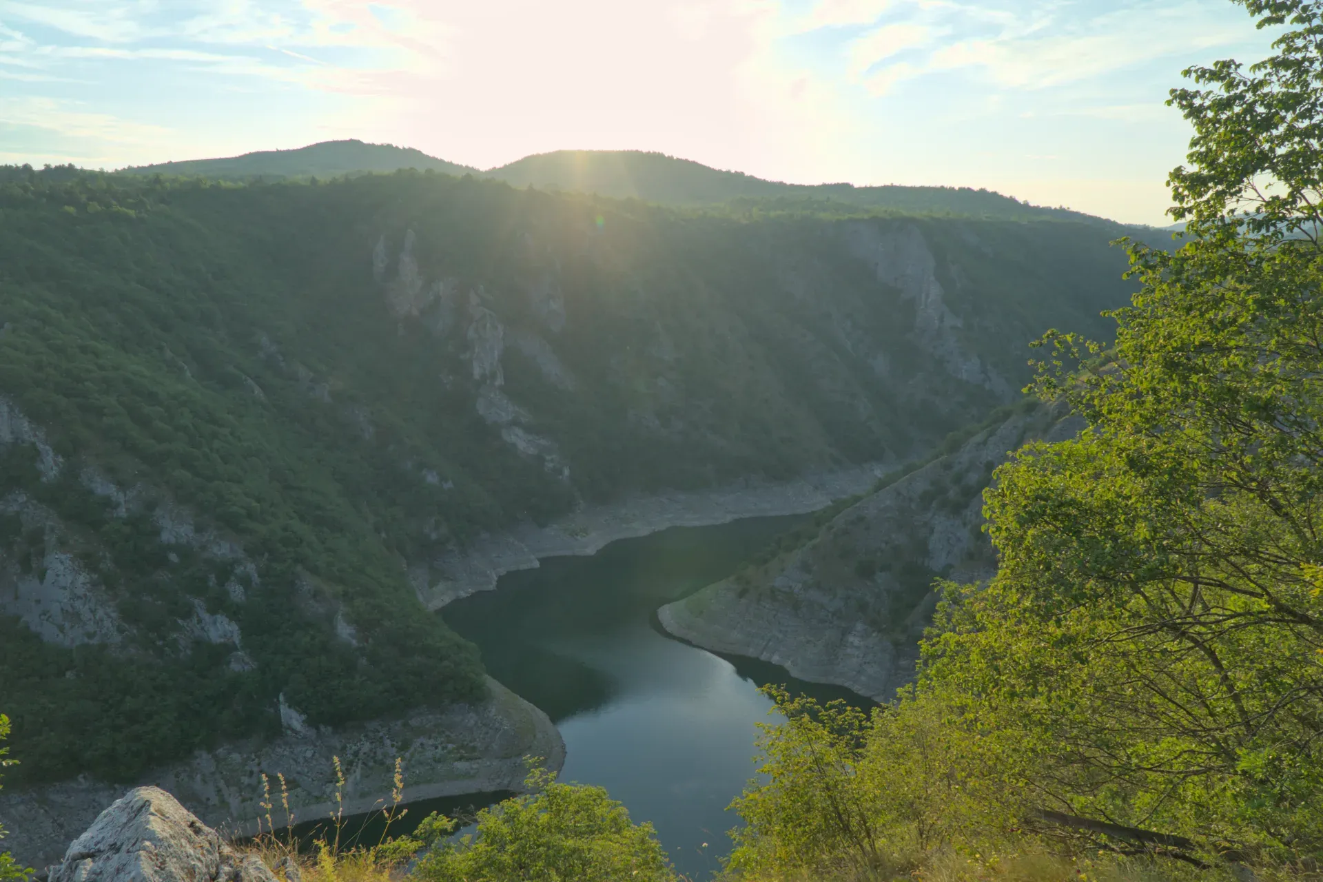 Meanders of the Uvac River at sunset, surrounded by green hills and rugged cliffs.