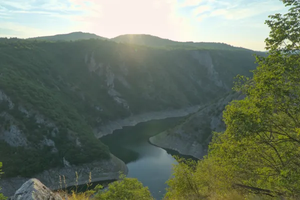 Meander des Uvac-Flusses bei Sonnenuntergang, umgeben von grünen Hügeln und zerklüfteten Klippen.