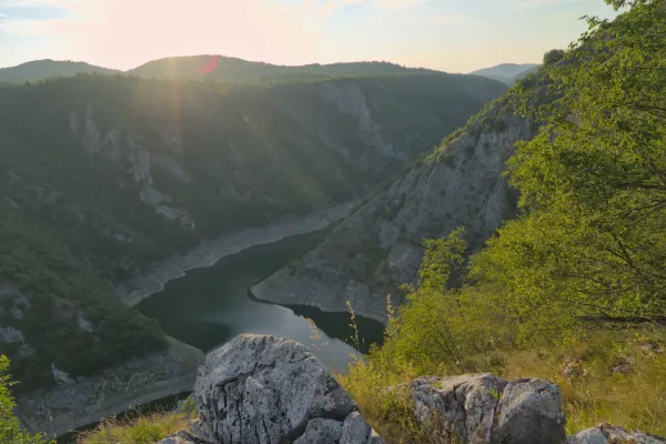 Malerische Aussicht auf die Uvac-Schlucht in Serbien, mit einem Fluss, der sich durch die bewaldeten Hänge schlängelt, beleuchtet vom warmen Abendlicht.