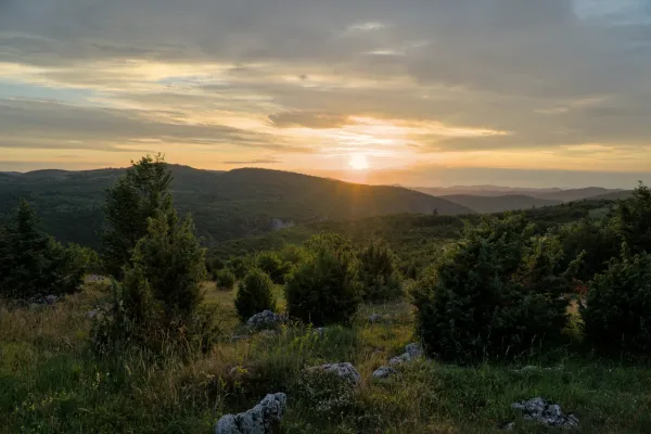 Zalazak sunca nad dolinom Uvac sa Vidikovca Mljetva, Srbija, sa dramatičnim oblacima i brdima okupanim suncem.