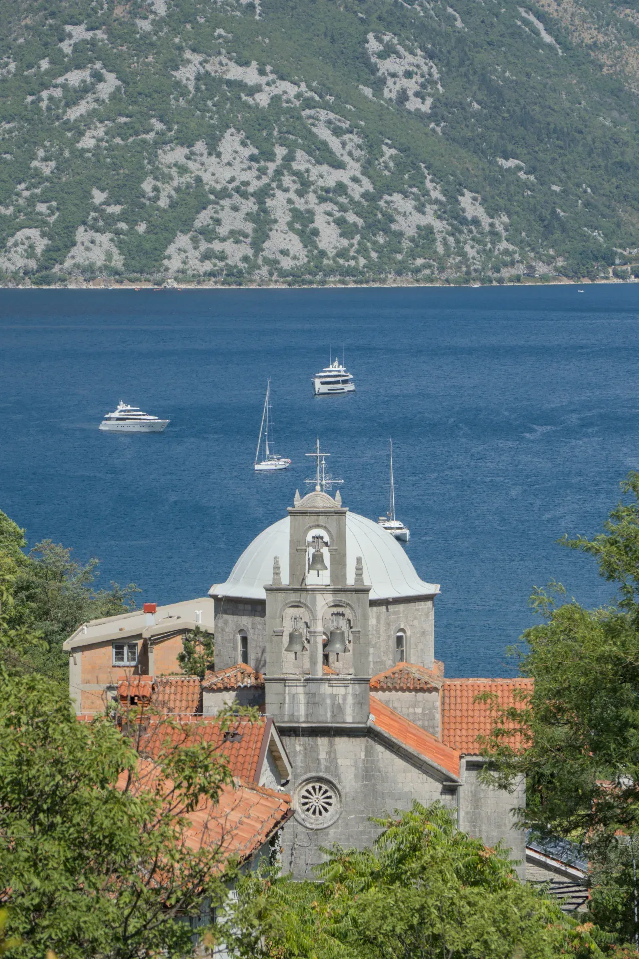 Scenic view of the Bay of Kotor in Morinj, Montenegro, with a church and yachts dotting the blue water.