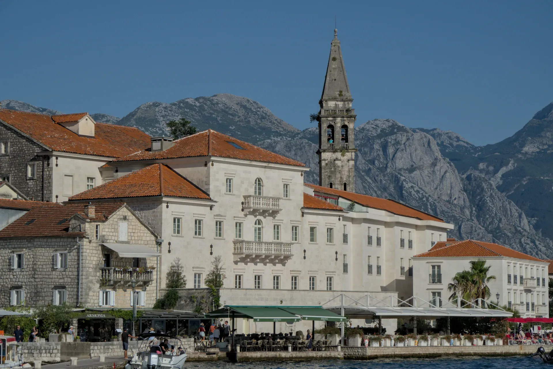 The picturesque town of Perast in Montenegro at sunset, with its historic buildings and bell tower against a mountainous backdrop.