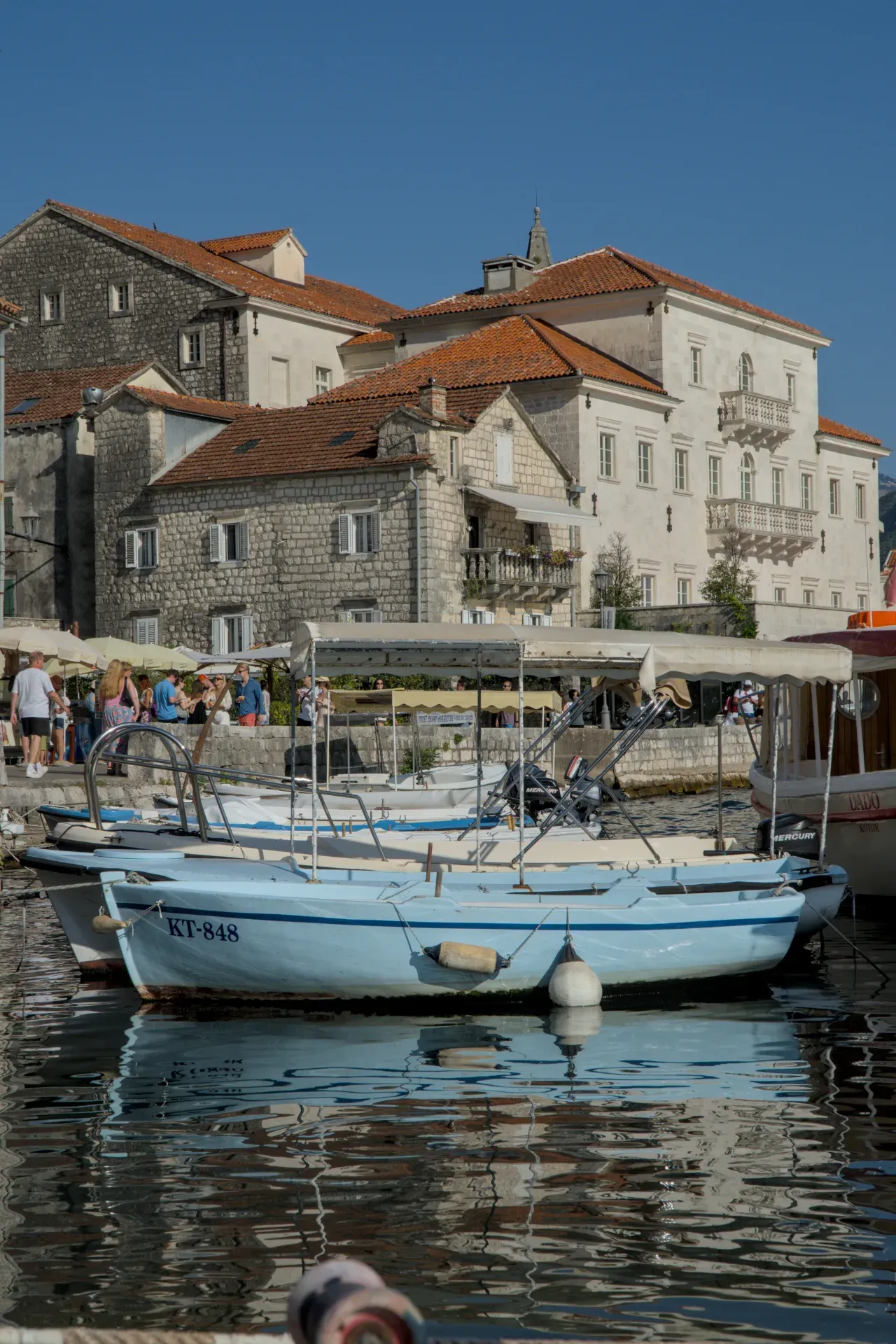 A blue boat is anchored in a picturesque harbor in Perast, Montenegro, with historic buildings in the background.