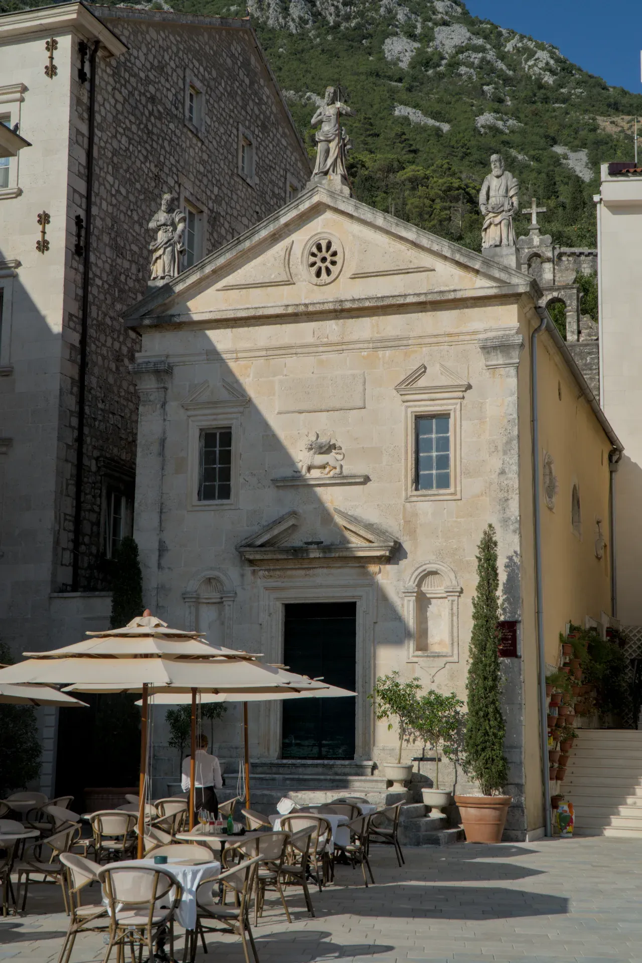 Evening view of the church in Perast, Montenegro, with surrounding buildings and outdoor seating.