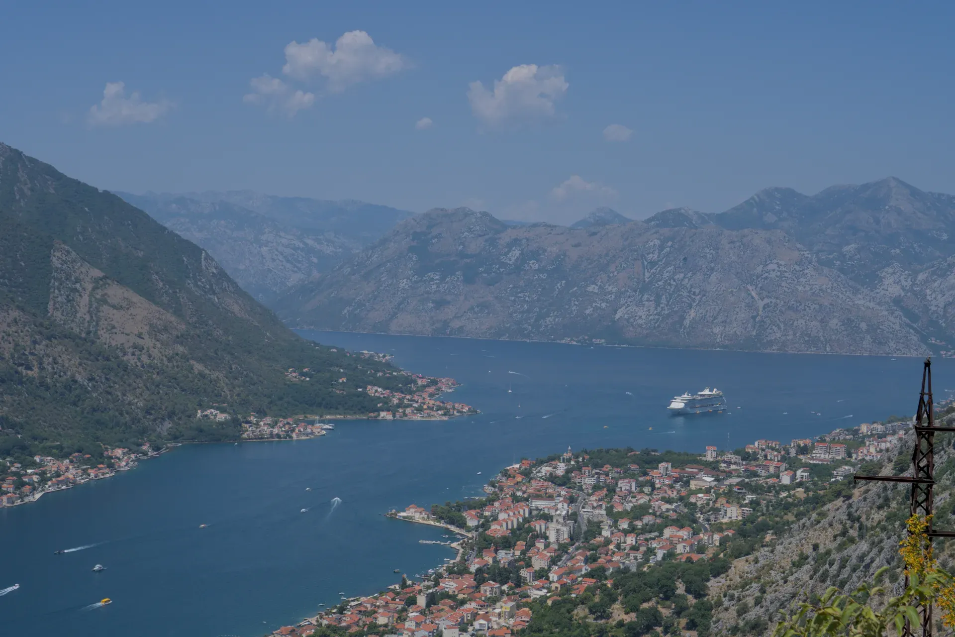 A large cruise liner gracefully enters the scenic Bay of Kotor, framed by mountains and a coastal town.