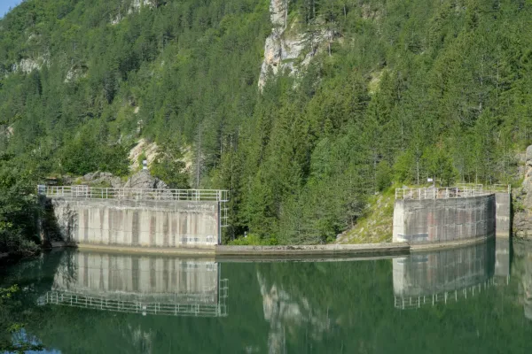 Дамба на озере Спайичи в Заовине, Сербия, отражается в спокойной воде, окруженная зелеными горами и лесом.