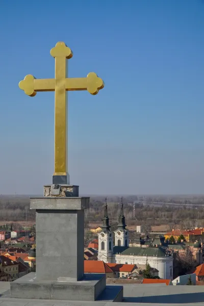 Ein goldenes Kreuz dominiert den Vordergrund mit einem Panoramablick auf Sremski Karlovci in Serbien im Hintergrund.