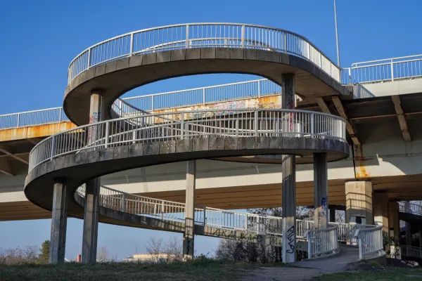 Una rampa a spirale in cemento con ringhiere metalliche, che scende dal Ponte della Libertà verso il Parco Kamenički.