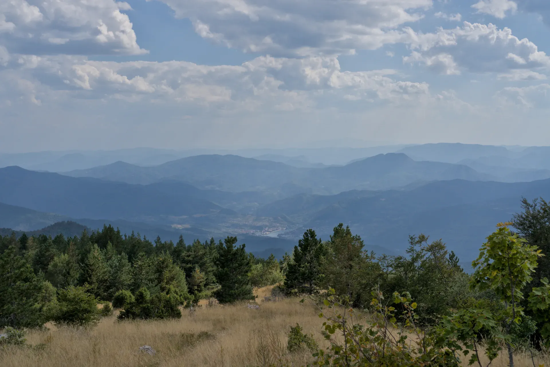 View of Višegrad from Janjač Mountain in Tara National Park, Serbia, featuring layered blue mountains and a cloudy sky.