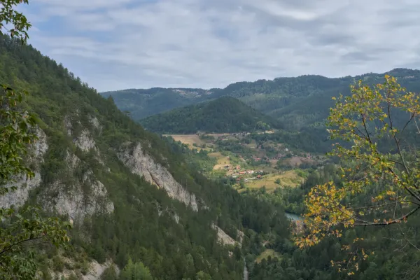 Panoramic view from Ravna Stena overlooking the village of Spaichi in Tara National Park, Serbia, featuring forested hills and a river.