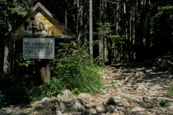 A rocky forest path leads towards Banjska Stena viewpoint in Serbia, with a sign urging nature preservation.