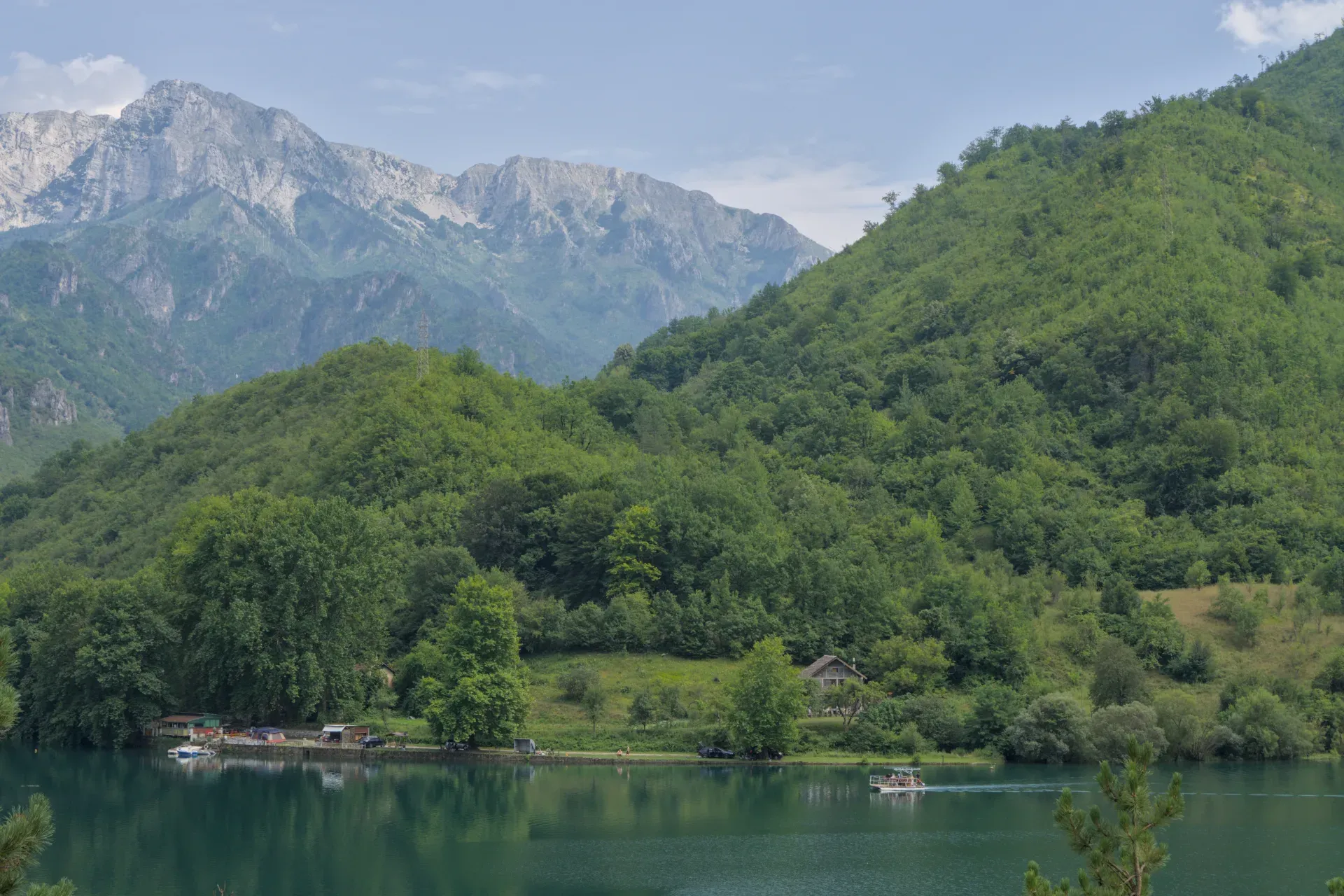 Scenic route from Sarajevo to Mostar: A mountain lake with a boat and green hills under a cloudy sky.