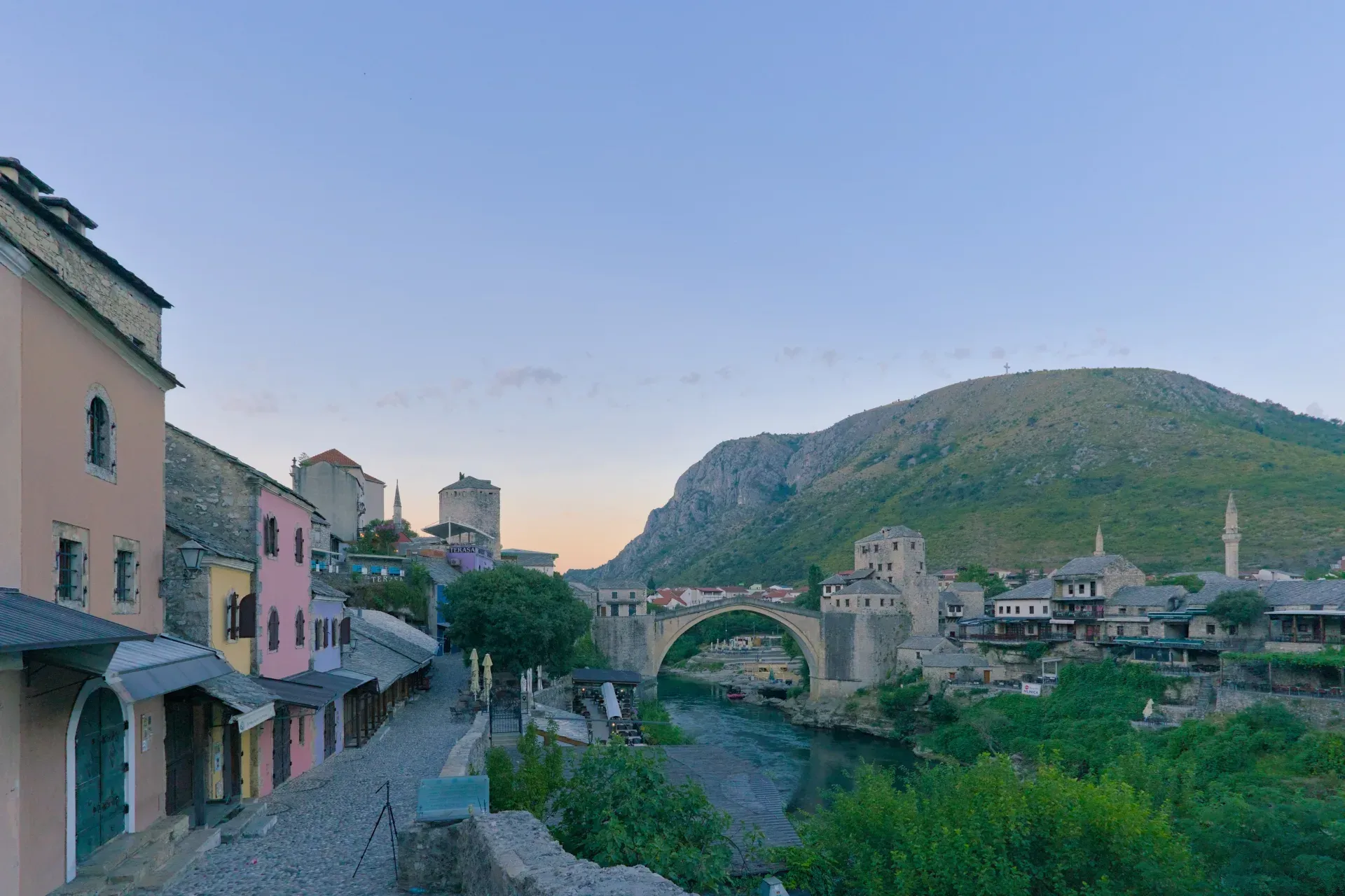 Pre-dawn panorama of Mostar's old town with colorful houses, the historic bridge, and a calm river.