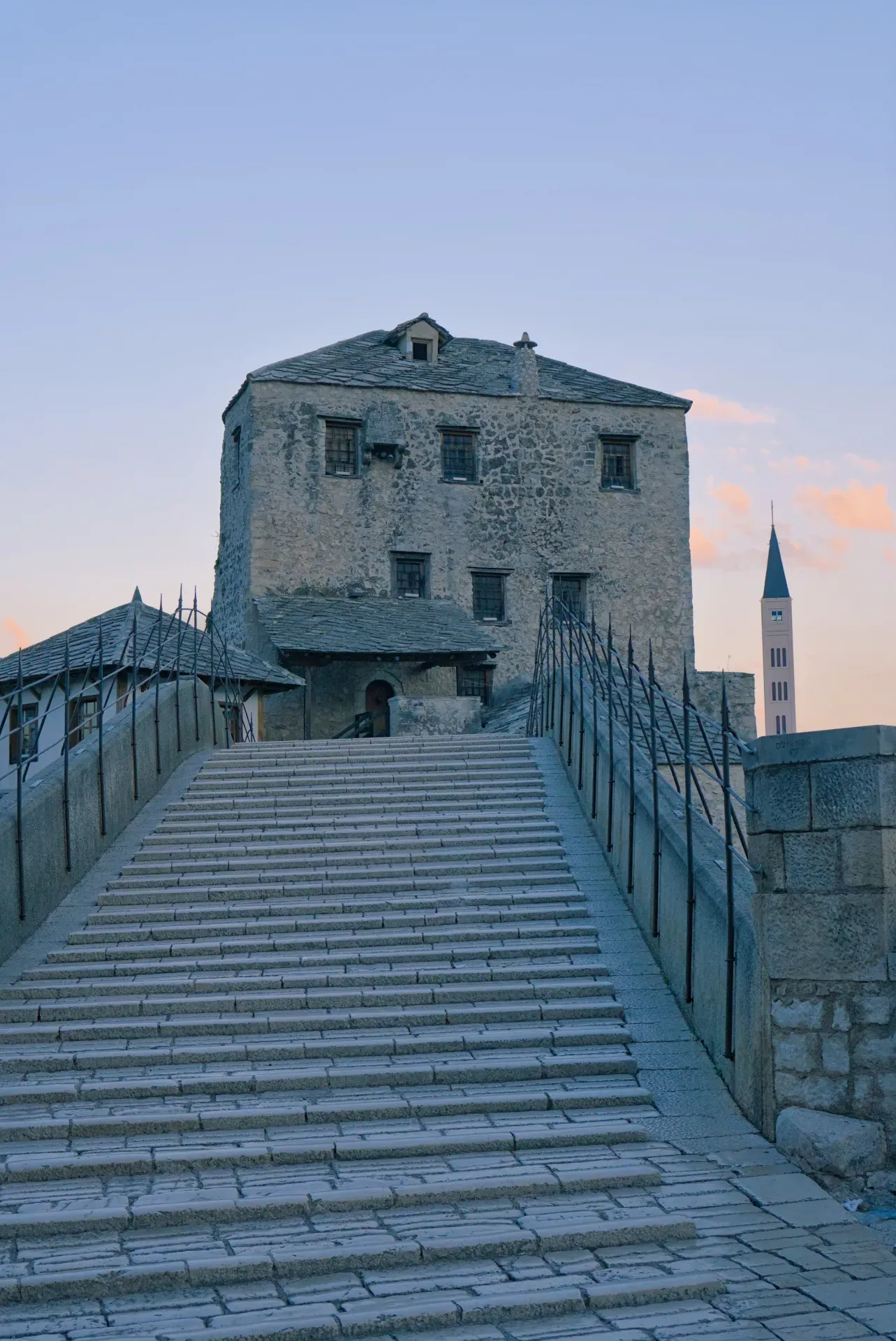 The old Stari Most bridge in Mostar at dawn, featuring stone stairs and historic buildings in the background.
