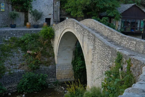 Steinbrücke mit einem einzigen Bogen, bekannt als "krumme Brücke", in Mostar, Bosnien und Herzegowina, umgeben von Grün.