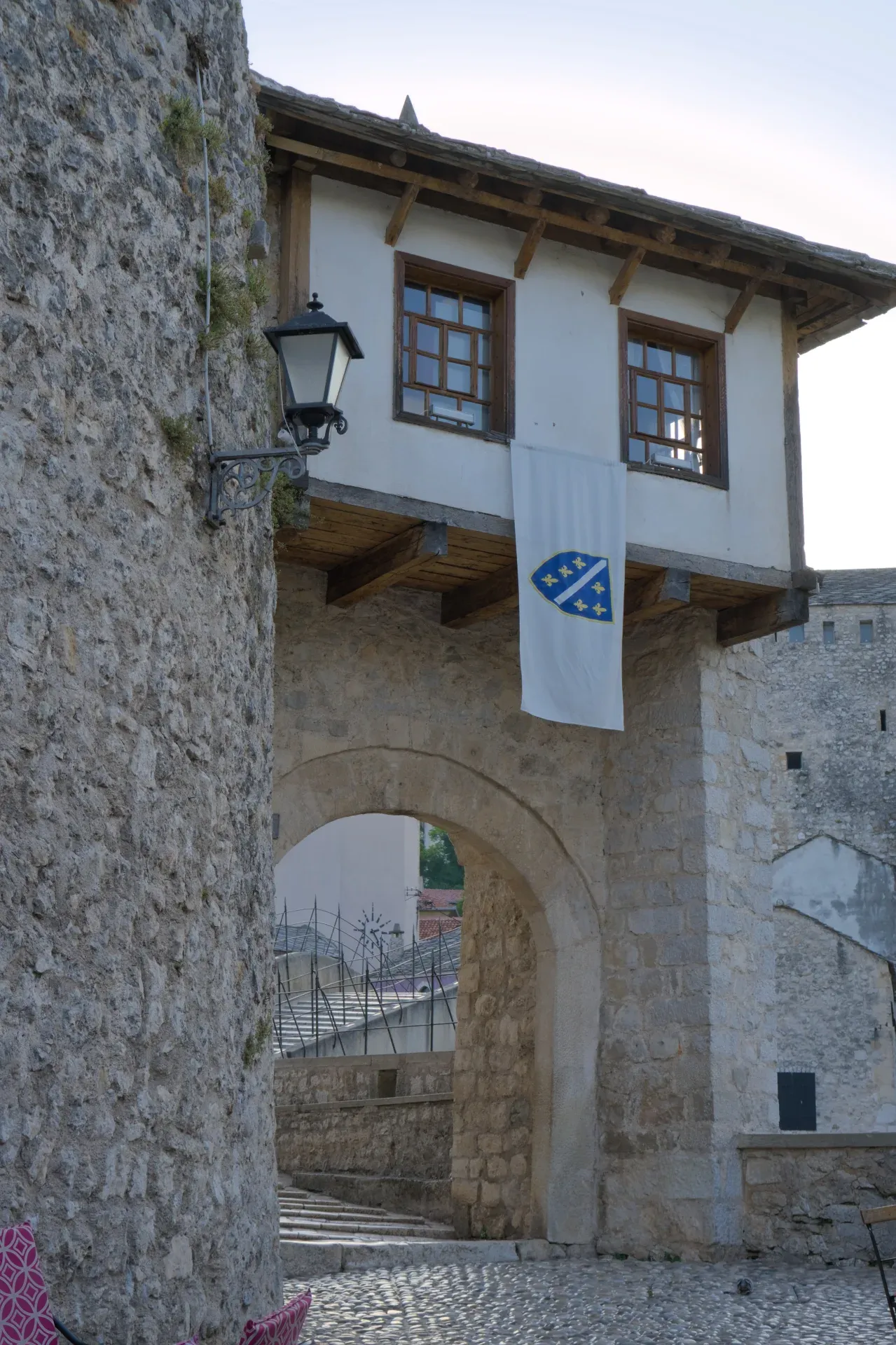 A stone tower stands prominently above the archway of the Old Bridge in Mostar, with a banner hanging.