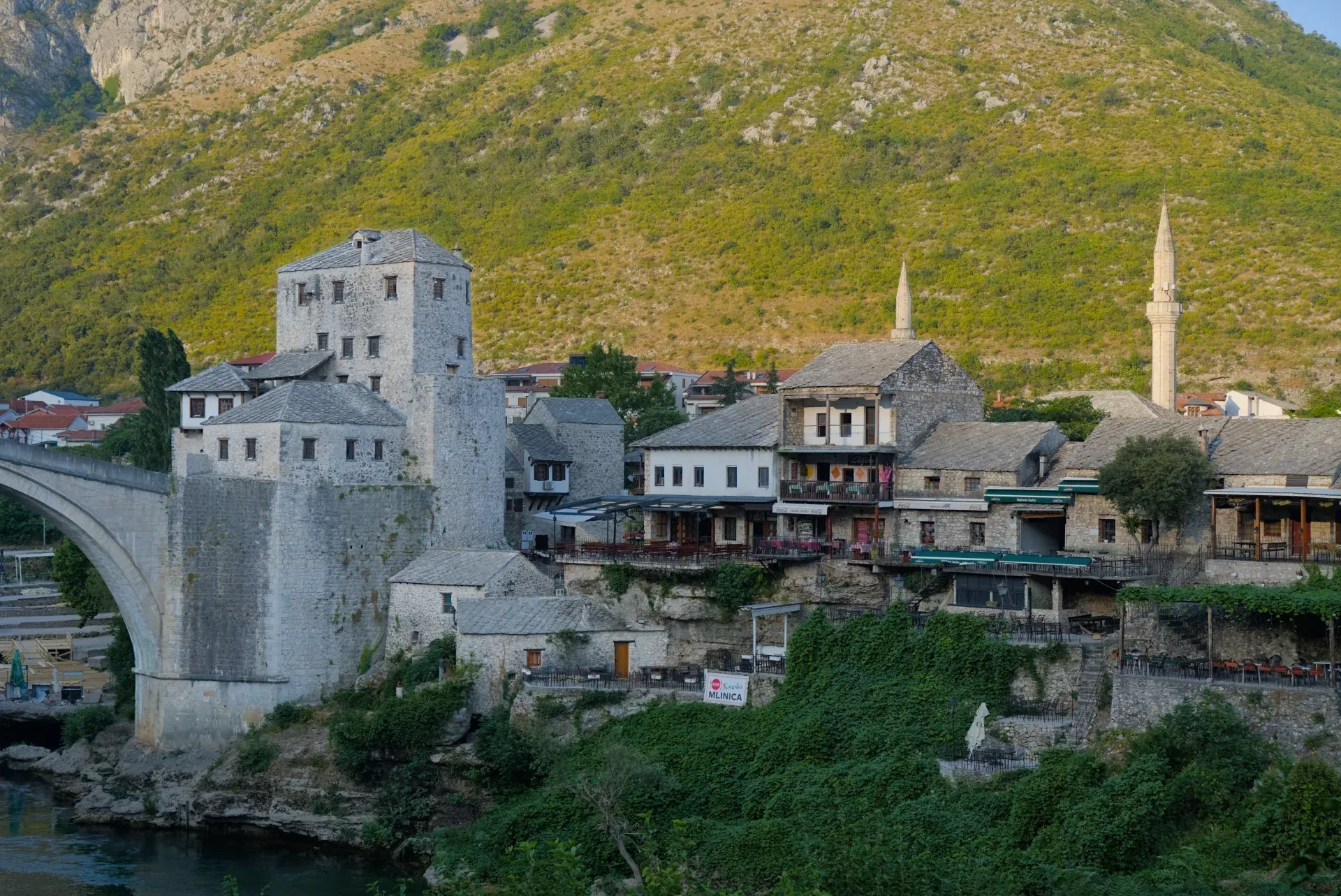 The old Mostar in golden sunrise light, featuring its historic stone bridge and surrounding buildings.