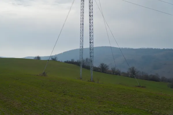 Un alto palo elettrico si erge sulle dolci colline verdi di Fruska, Serbia, sotto un cielo coperto.