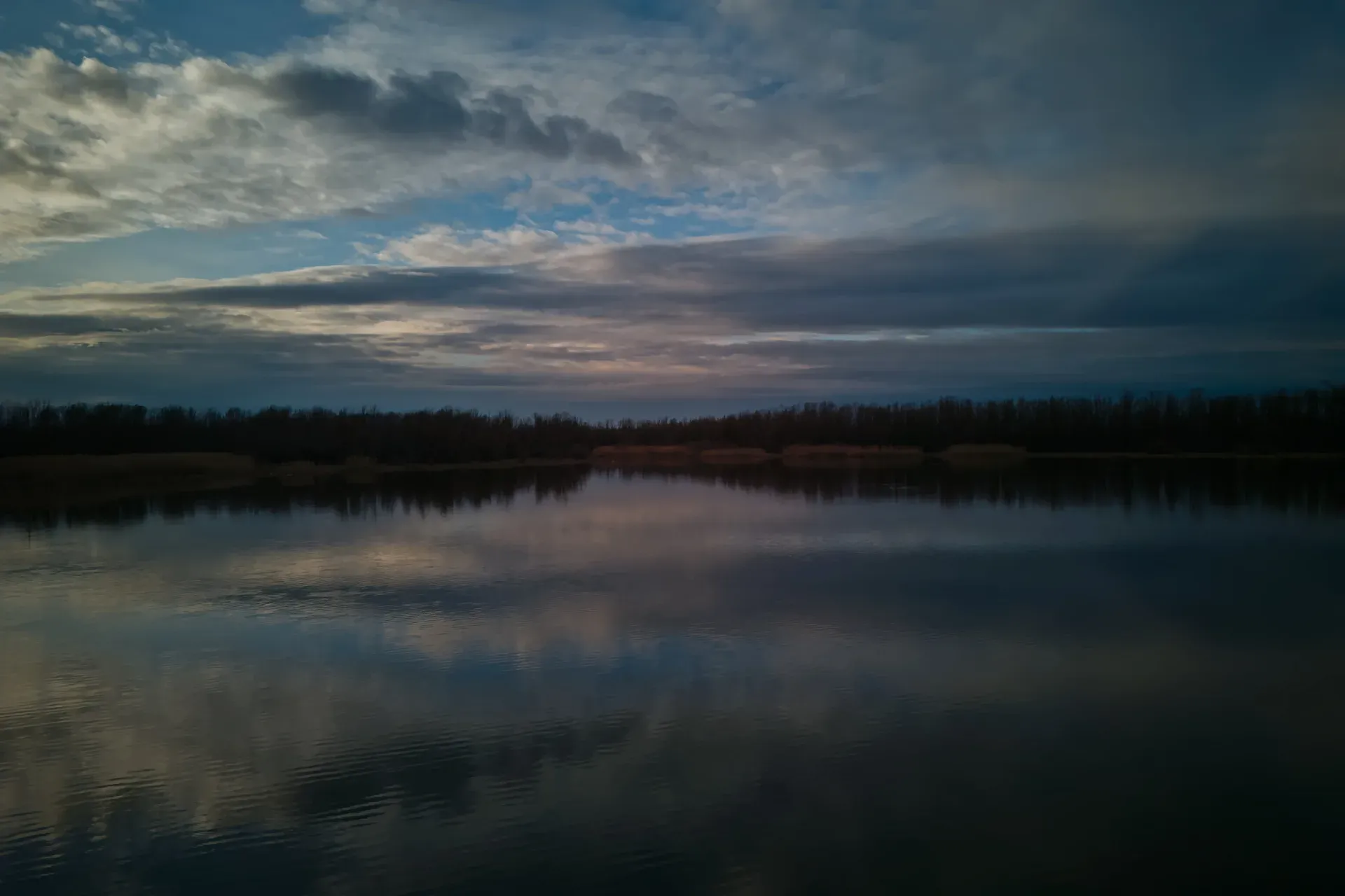 Begečka Jama avant le coucher du soleil, avec des nuages dramatiques reflétés sur la surface de l'eau calme.