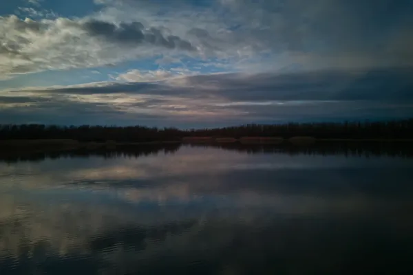 Begečka jama pred zalazak sunca, sa dramatičnim oblacima koji se ogledaju na mirnoj površini vode.