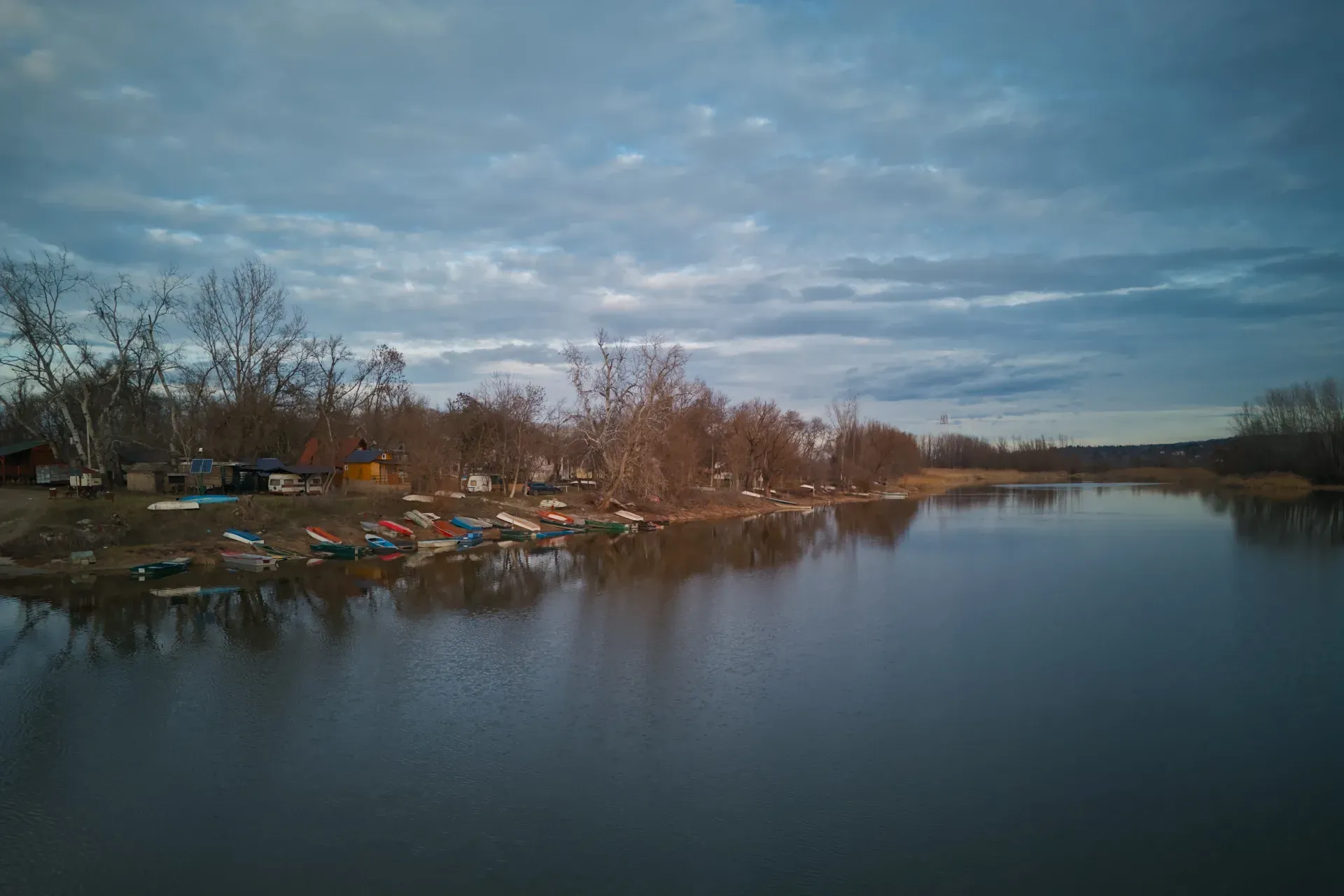 Des bateaux reposent sur le rivage serein de Begečka Jama, Novi Sad, Serbie, sous un ciel nuageux et dramatique.