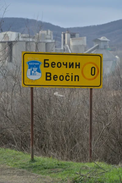 Žuti putokaz za "Beočin" na srpskom i latiničnom pismu sa fabrikom cementa u pozadini.