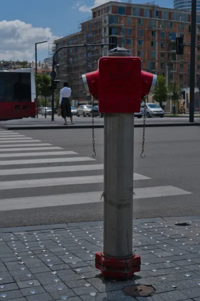 Un hydrante rouge se dresse sur une rue pavée de Belgrade, à côté d'un passage piéton et d'un bâtiment inachevé.