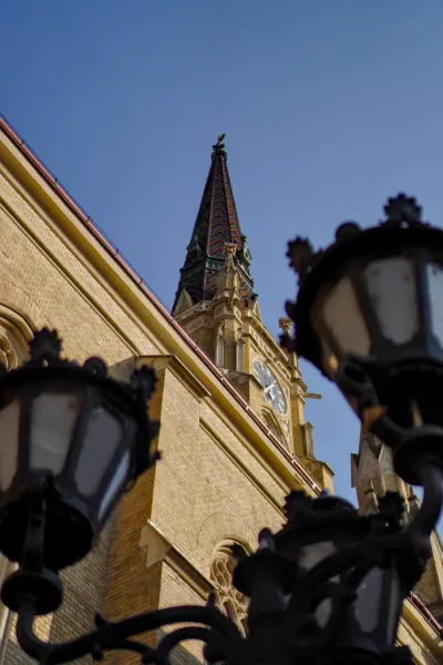 Fotografija Hrama Device Marije u Novom Sadu, Srbija, sa krovom od crepova i satom, snimljena iz niskog ugla.