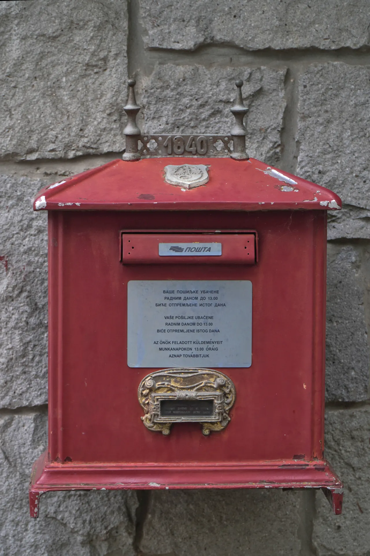 Red vintage mailbox with '1840' and 'POŠTA' inscription on a stone wall in Palic, Serbia.