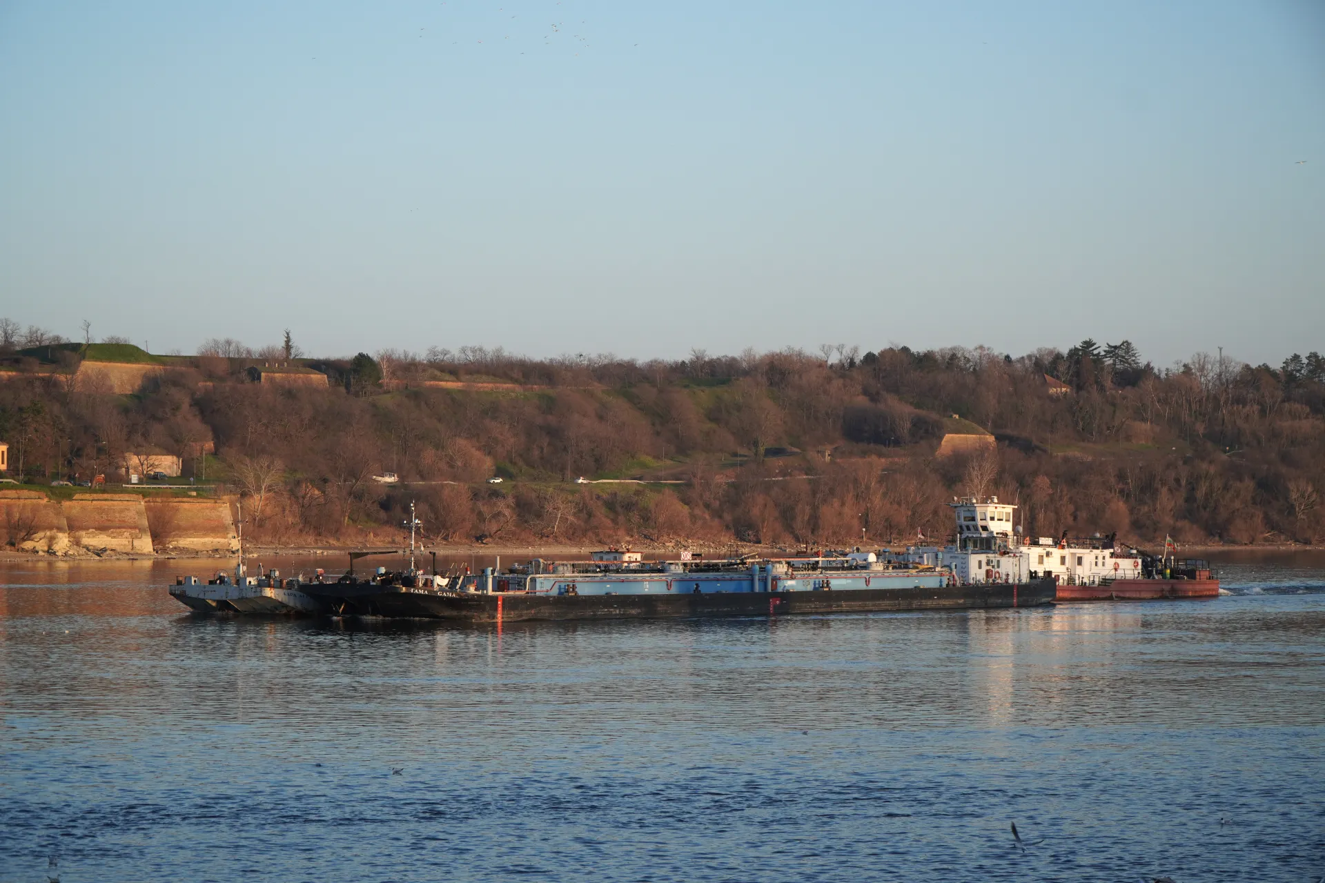 Two barges are sailing on the Danube River in front of the Petrovaradin Fortress in Novi Sad, Serbia.