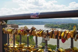 A railing filled with colorful love locks overlooks the Danube River and the city of Novi Sad, Serbia, seen from Petrovaradin Fortress.