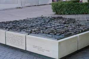 A detailed bronze model of the city of Zagreb, Croatia, with buildings and streets, placed on a concrete pedestal with inscribed text. A green hedge is visible in the background.