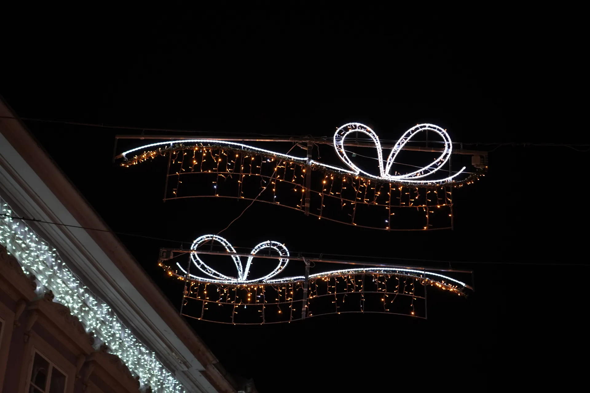 Two illuminated gift box decorations with white and orange lights hanging over a dark background in Novi Sad, Serbia.