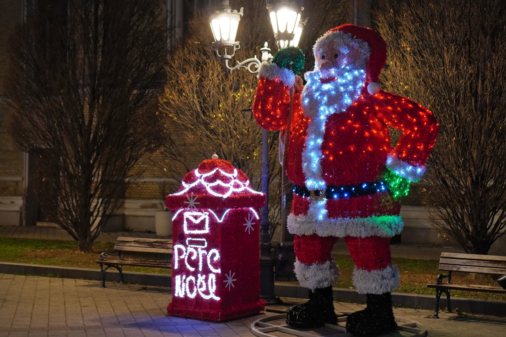 A large, illuminated Santa Claus figure stands next to a red mailbox with 'Père Noël' written in lights, decorated for Christmas in Novi Sad, Serbia.
