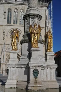 Golden statues of angels on a stone monument with Zagreb Cathedral in the background.