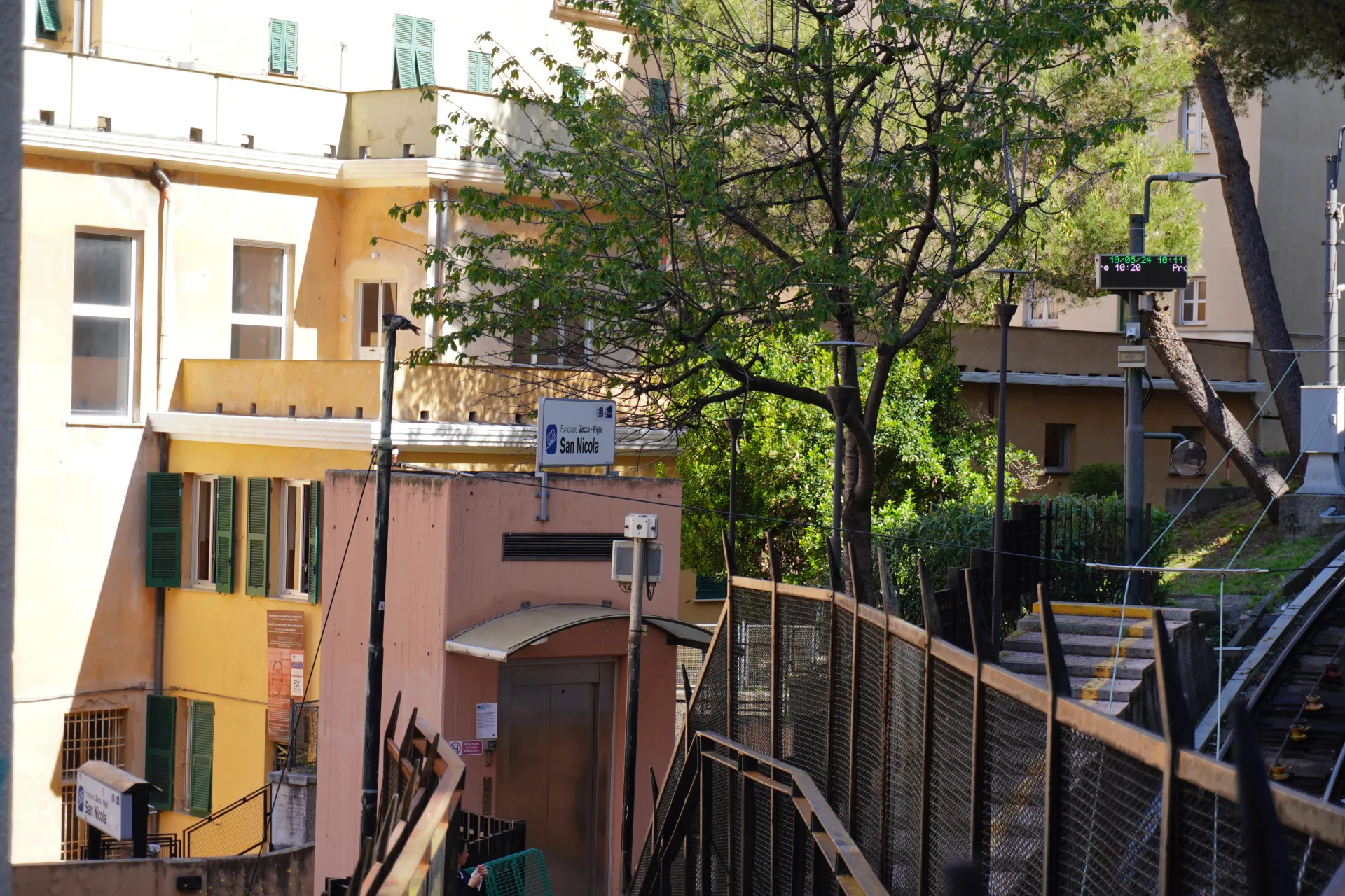 Pogled na zgradu stanice žičare San Nikola u Đenovi, Italija, sa fasadom boje breskve, modernim liftom i znakom za Funicolare Zecca - Righi.