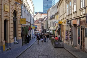 A view down Tkalčićeva Street in Zagreb, Croatia, with people walking on a cobblestone street lined with shops and buildings.
