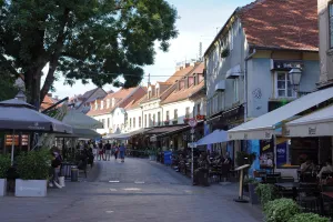 A bustling pedestrian street in Zagreb, Croatia, with outdoor cafes, shops, a large tree, and people enjoying the day.