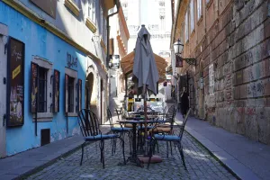 Outdoor seating of a cafe on a cobblestone street in Zagreb, Croatia, with blue and brick buildings on either side.