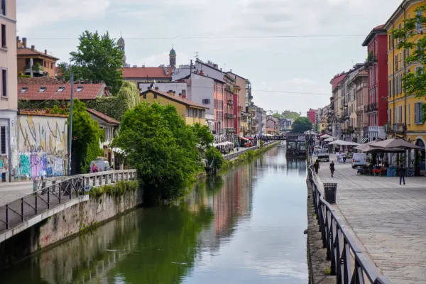 Un canal en el distrito Navigli de Milán con edificios coloridos, una estructura flotante llamada 'Square Garden', un barco y una motocicleta.