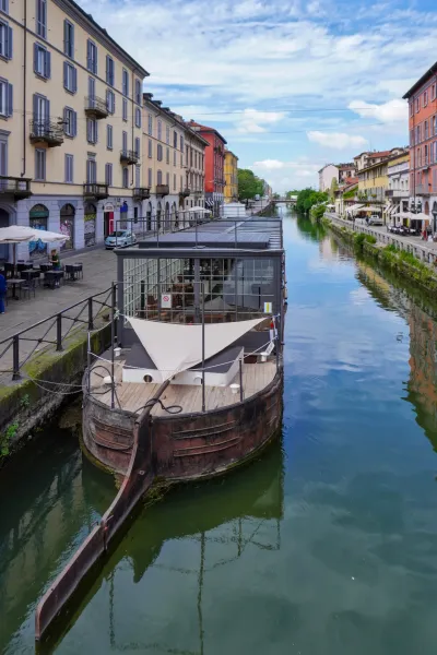 Ein Blick auf die Navigli-Kanäle in Mailand, Italien, mit bunten Wohngebäuden entlang der Wasserstraße und Fahrrädern, die am steinernen Gehweg geparkt sind.