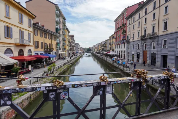Gente remando en barcos por un canal bordeado de edificios históricos y restaurantes al aire libre en el distrito Navigli de Milán.