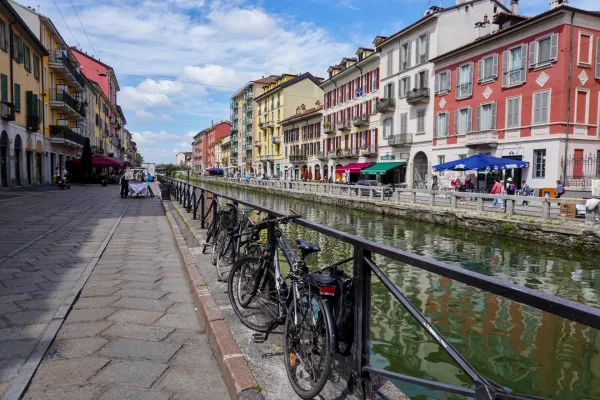 Un canal en el distrito Navigli de Milán con barcas de dragón compitiendo, flanqueado por edificios coloridos y asientos al aire libre.