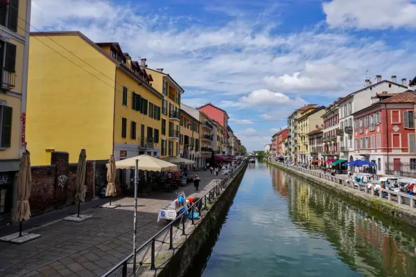 Un día soleado en el distrito Navigli de Milán, mostrando un canal con edificios y gente en barcos.