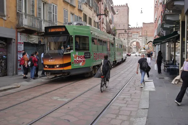 Un tranvía amarillo en una calle empedrada en Milán con edificios y cafés a los lados.